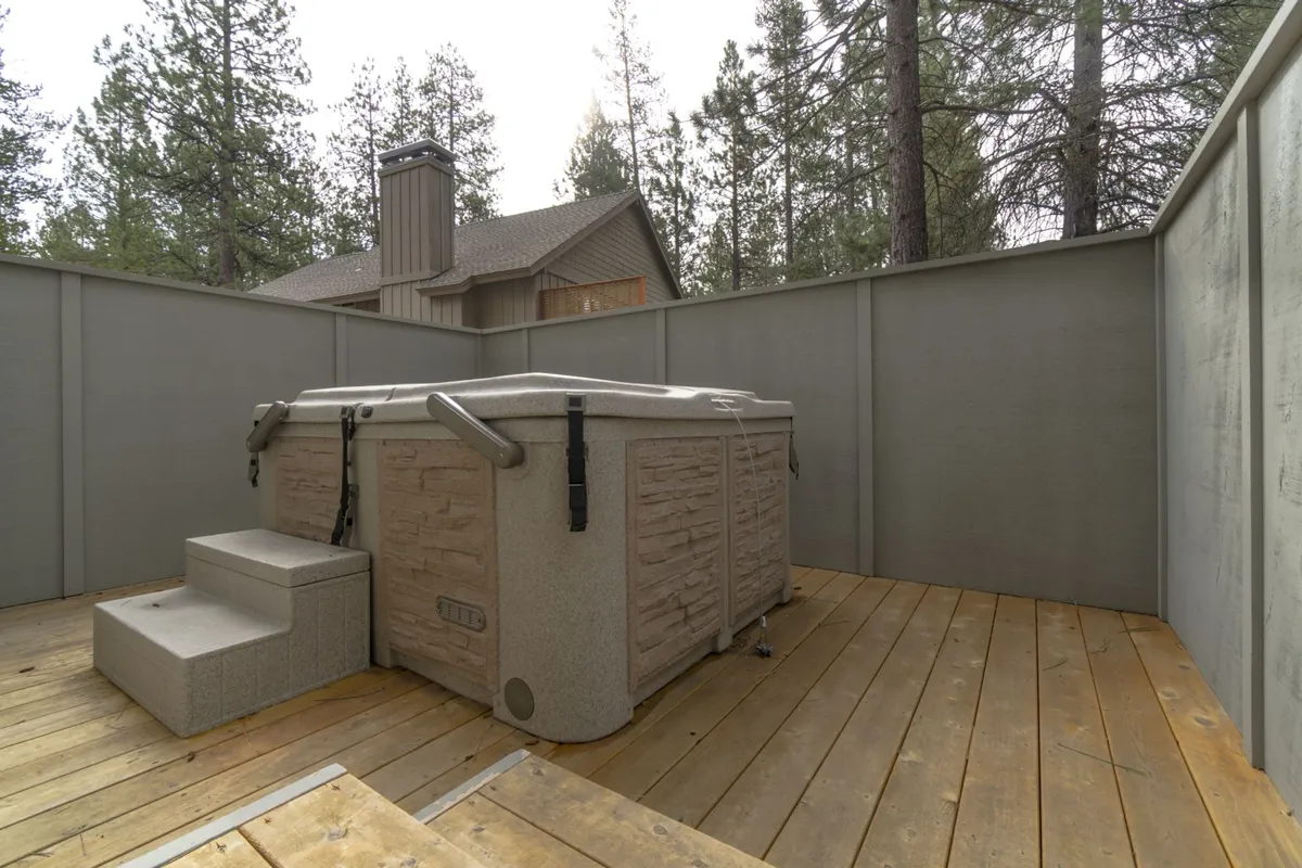 A serene outdoor hot tub set on a wooden deck, surrounded by tall trees. The setting is peaceful, perfect for relaxing sore muscles after a day of recreation, with the promise of beautiful sunsets or stargazing in the fresh mountain air.