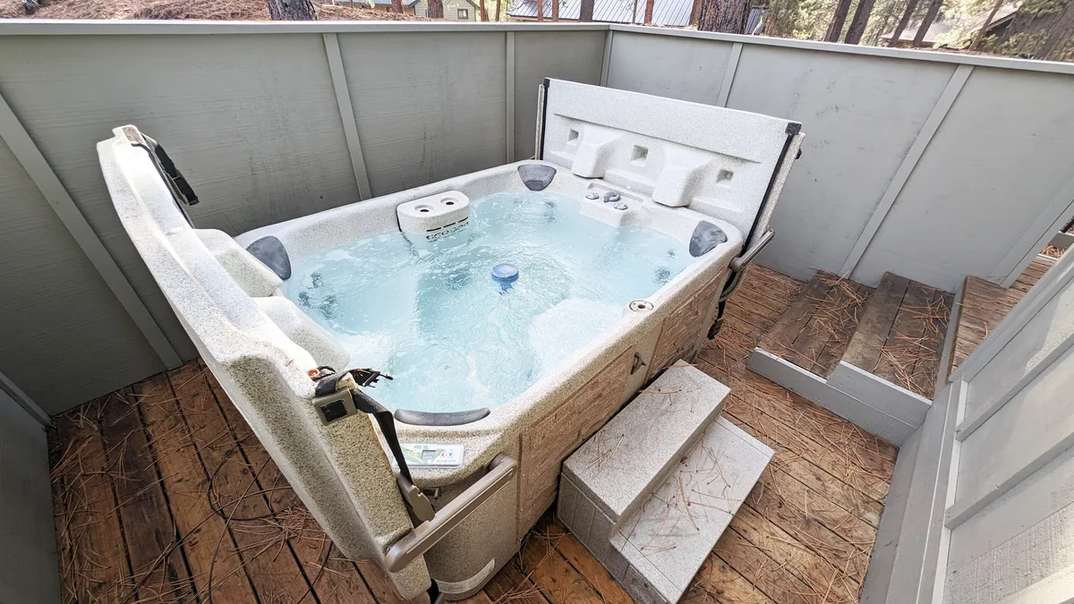 This image features a bubbling hot tub set into a wooden deck, with steps leading up to the tub, surrounded by tranquil natural scenery. The setting evokes a calm, inviting mood, perfect for relaxing under the stars or enjoying social moments with friends and family.