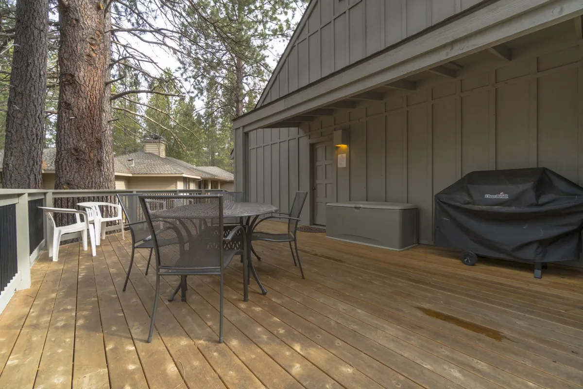 This exterior shot showcases a wooden deck with an outdoor dining table and grill, surrounded by tall, leafy trees. The space is set up for casual meals and socializing in the fresh air, evoking the feel of summer gatherings or family barbecues after a day of adventure.