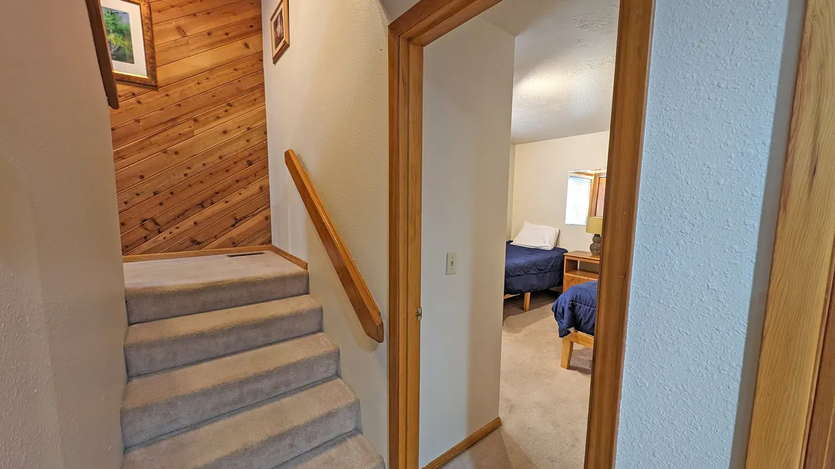 A warmly lit staircase area with wood paneling and a partial bedroom view. The space exudes a welcoming ambiance, suggesting quiet evenings and restful transitions between the living spaces and sleeping quarters.