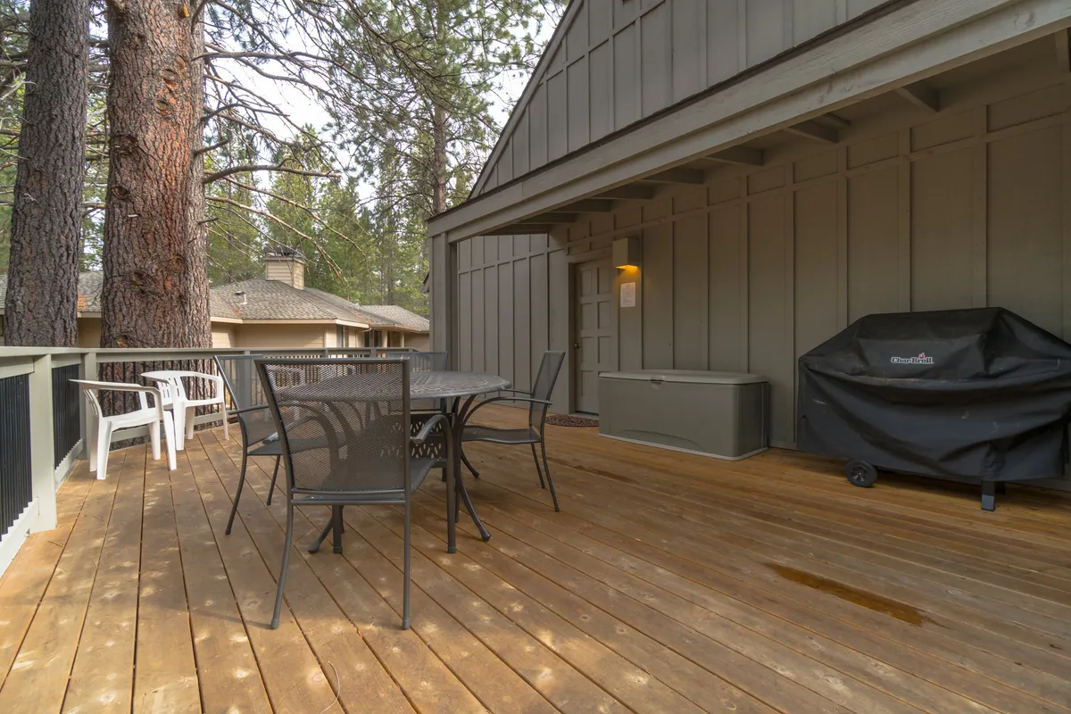 Depicts a wooden deck with a dining table and chairs, a barbecue grill, and tall trees providing a lush natural backdrop. The setting is ideal for casual outdoor meals, morning coffee, or sunset dinners, perfectly blending comfort with the outdoors.