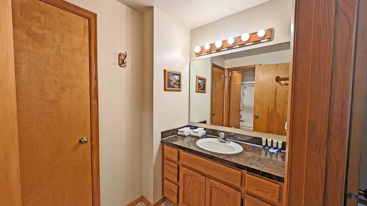 A bright and serene bathroom with a vanity, sink, mirror, wooden cabinets, and framed photos. The space exudes calm and relaxation—ideal for morning routines or winding down with a relaxing bath.