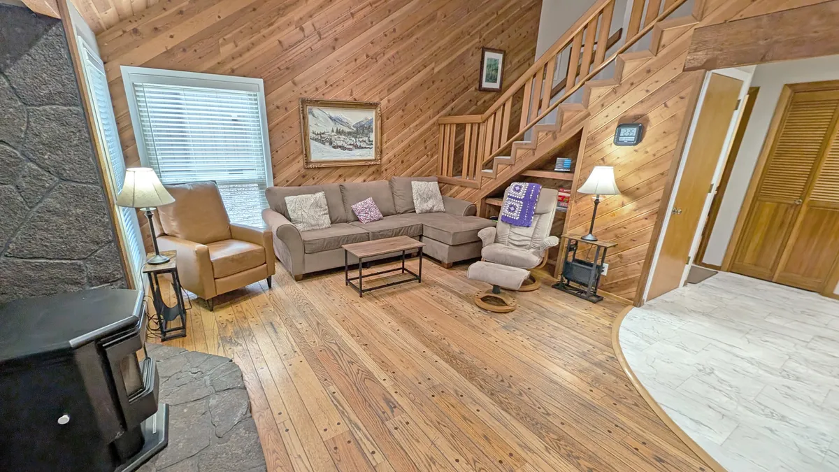 This image features a comfortable sofa, a wooden staircase, and a stone fireplace, all bathed in warm light. The space feels open and relaxed, with artwork on the wall, suggesting a homey gathering spot for family and pets after a day outside.