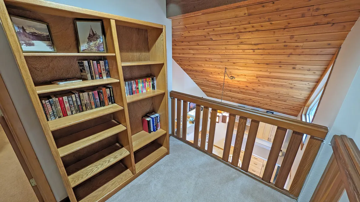 A wood-paneled loft with a prominent bookshelf and sloped ceiling, perfect for curling up with a book or sharing a quiet conversation. The inviting atmosphere is ideal for couples or small groups seeking relaxation and connection.